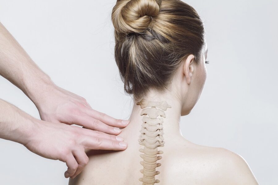 A therapist's hand resting along a client's neck and upper back, with the cervical spine illustrated over the shoulders.