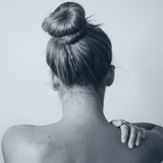 A person reaching back to hold a tight neck and shoulder.